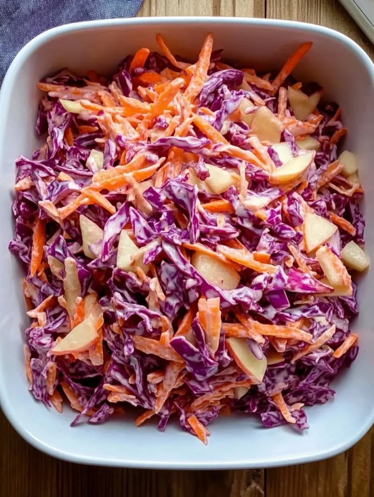 A large white bowl filled with colorful Cabbage Carrot Apple Slaw, showing shreds of red cabbage, orange carrots, and pieces of apple in a creamy dressing.