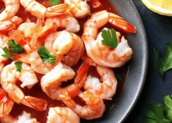 A delicious shrimp cocktail served in a glass with zesty sauce and lemon.