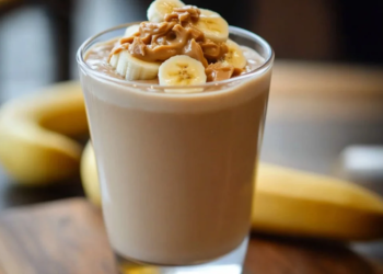 A creamy Peanut Butter Banana Smoothie in a glass, topped with banana slices and a straw.